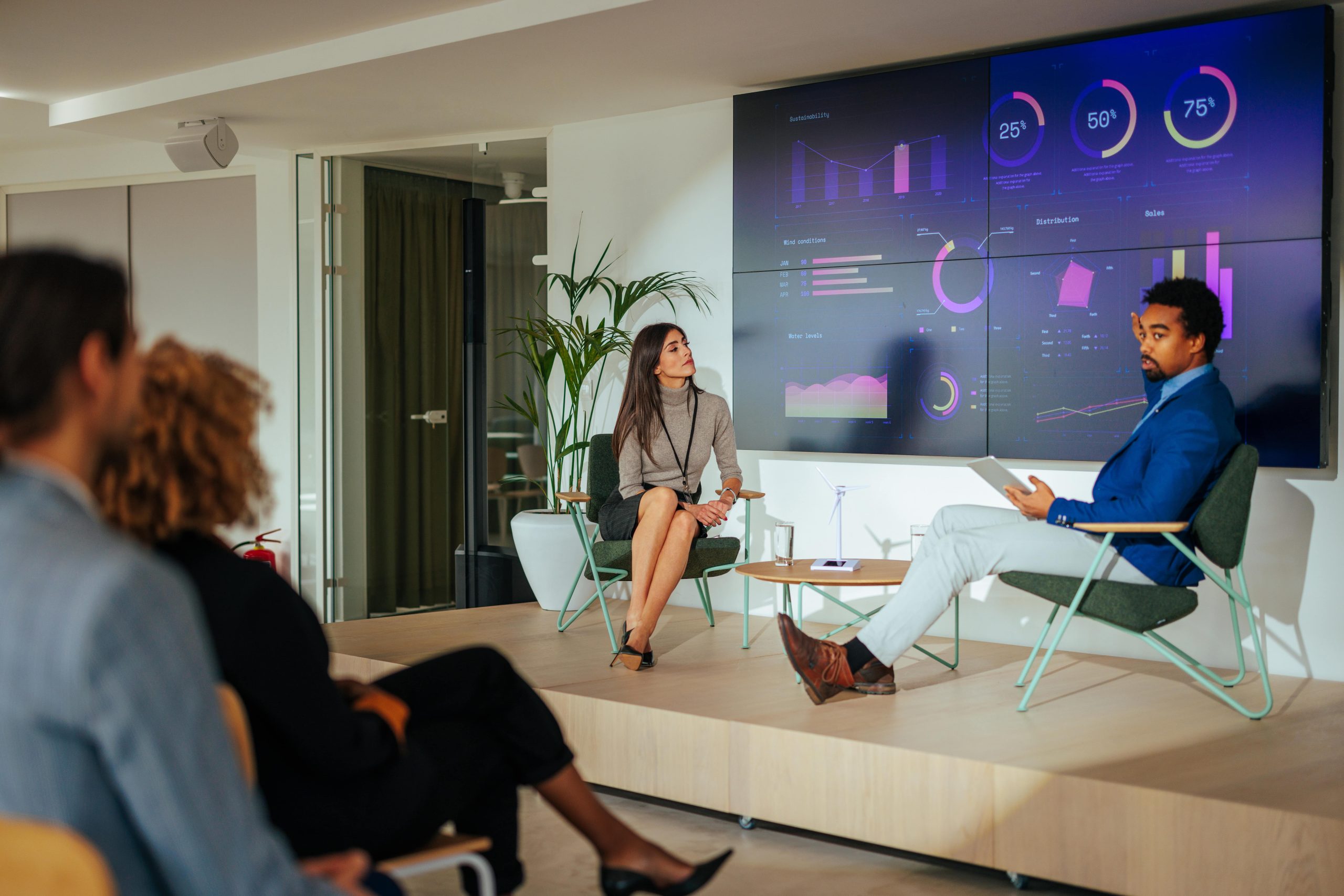 People in a casual office meeting with a presentation on a large screen.